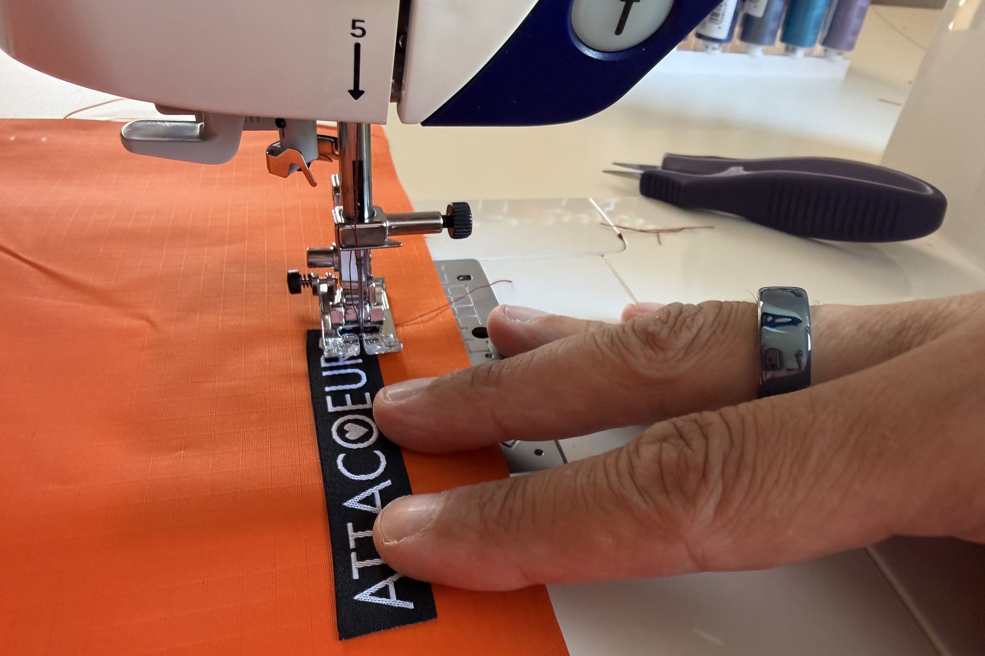 Sewing the woven ATTACOEURS label onto orange ripstop